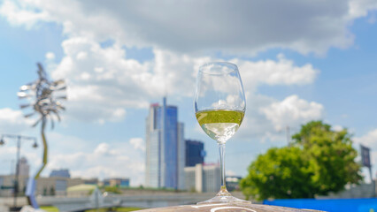 Glass of white wine with reflection on the blurred cityscape and dramatic sky background. Space for text. Wine concept.