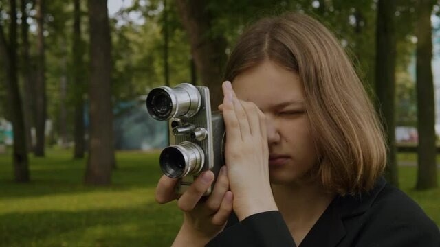 Close up vintage movie camera.Portrait of a Teenage blonde girl shoots with a vintage movie camera around herself.Against the background of a green park.