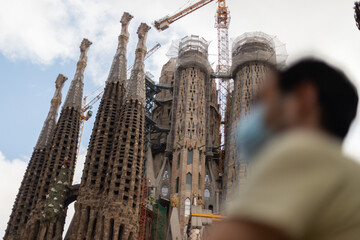 Young man with a medical face mask in front of the Sagrada Familia basilica in Barcelona, Spain...