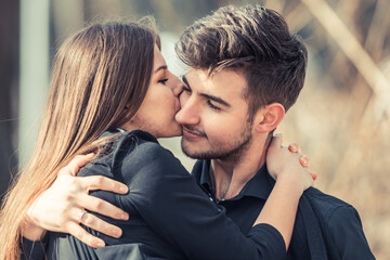 Loving happy couple in love smile and kiss his cheek outside. Love story concept