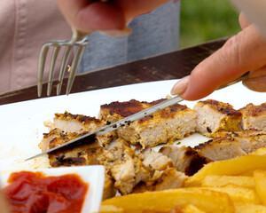 The moment of cutting meat on a white plate during a hearty lunch.
