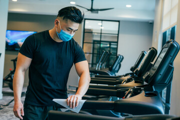 Asian male wearing mask during COVID19 wiping down treadmill