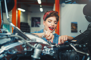 Naklejka na ściany i meble beautiful girl repairs a motorcycle in a workshop, pin-up style, service and sale