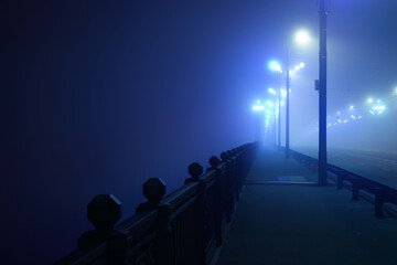 Pedestrian walkway through the illuminated empty Stone bridge in a thick fog at night. Lanterns...