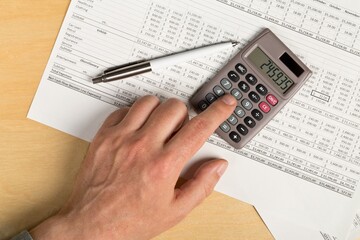 Man using pocket calculator with pen on financial analysis sheet background on wooden office desk -...