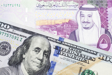 A close up image of a one American one hundred dollar note close up in macro with a colorful five Saudi riyal bank note from Saudi Arabia