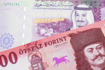 A close up image of a red, one hundred Hungarian forint bill close up with a colorful five riyal...