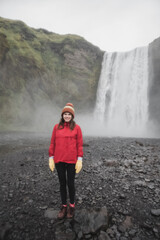 Iceland landscape photo of brave girl who proudly standing with his arms raised in front of water wall of mighty waterfall.