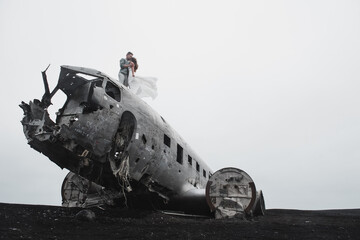 young couple holding hands together and coming to the old plane on the ground black beach in Iceland