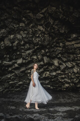bride in white clothes stands in a black cave on a black sand beach near the Atlantic Ocean in Iceland