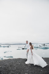 Fototapeta na wymiar Wedding in Iceland. A guy and a girl in a white dress are hugging while standing on a blue ice floe on a background of mountains