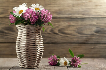 Bouquet of wildflowers, daisies and clover in a wicker vase on a wooden background. Image with copy space for postcard or design