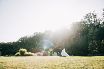 Bride and Groom at wedding Day walking Outdoors on summer green nature. Bridal couple, Happy Newlywed woman and man embracing and kissing in green park. Loving wedding couple outdoor. Bride and groom