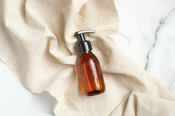 Amber glass brown pump bottle with beige fabric on marble background. Cosmetic packaging mockup....