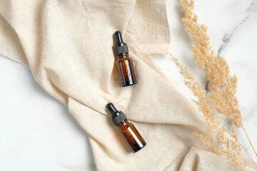 Amber glass essential oil brown bottles with beige fabric and dry flowers on marble background. Flat lay, top view. Natural organic beauty product packaging mockups.