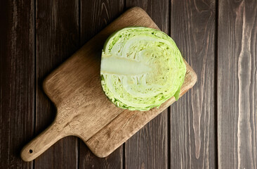 Half a head of fresh white cabbage on wooden cutting board over dark table background.