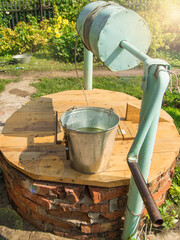 Metal bucket on a wooden lid of a brick well, open on a Sunny summer day