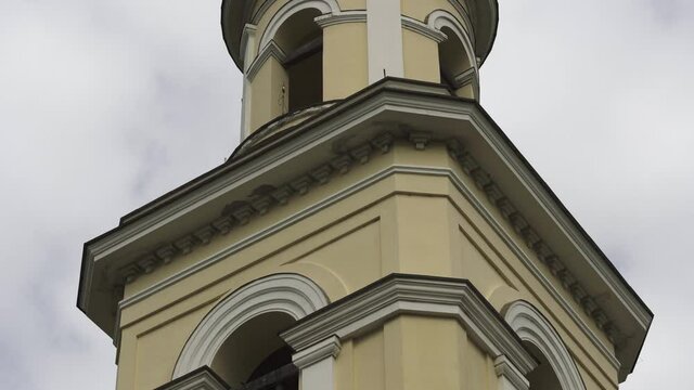 Concept of religion and faith. Stock footage. The high white and yellow bell tower of the Orthodox Church with a golden cross on blue cloudy sky background.