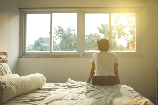 Young woman sits on bed while enjoys sunset view - Powered by Adobe