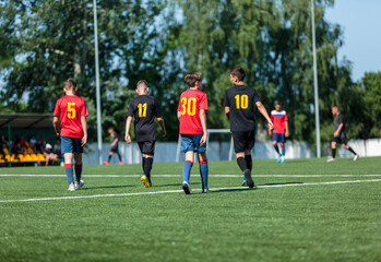 Boys in red and black sportswear plays football on field, dribbles ball. Young soccer players with ball on green grass. Training, football, active lifestyle for kids	