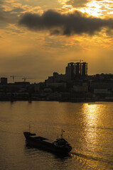 Cargo ship silhouette and in sunset light with a cityscape on background. Golden Horn Bay, Vladivostok, Russia