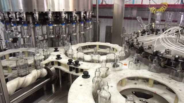 Factory for bottling vodka. Working machine with conveyor line for production of alcoholic beverages. Glass bottles in conveyor belt in distillery production line.