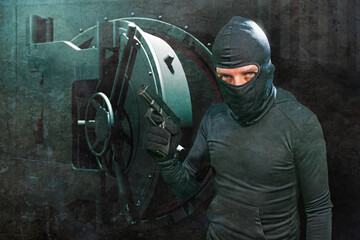 heist and robbery - Hollywood style portrait of man in balaclava mask holding gun in front of security metal vault door in bank or casino heist concept stealing money