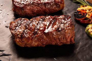 Grilled sliced beef steak on cutting board on black board over wooden table.