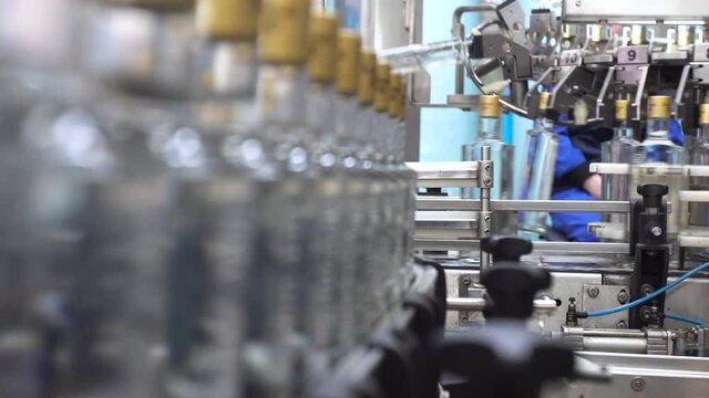 Factory for bottling vodka. Working machine with conveyor line for production of alcoholic beverages. Glass bottles in conveyor belt in distillery production line.