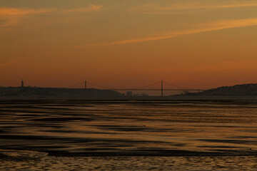 Low light image taken at sunset on the banks of Tagus River that lies between Almada and Lisbon. It features silhouettes of both cities, the 25 de abril suspension bridge and Christ the king monument.