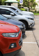 Closeup of front side of red car with other cars parking in outdoor parking area in bright sunny day. Vertical view.
