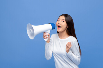 Cheerful cute Asian woman talking on magaphone isolated on blue background