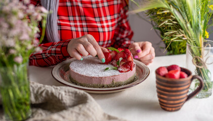 Woman is decorating a delicious strawberry mousse cake with berries. Concept of tasty and healthy summer desserts