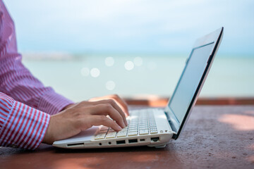 Woman hand using laptop to work study on work desk with clean nature beach outdoor background. Business, financial concept.