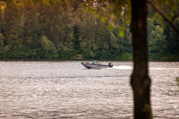 A black and gray speedboat navigates in front of the tender green trees the Dnieper river in Kiev, Ukraine, at the beginning of summer.