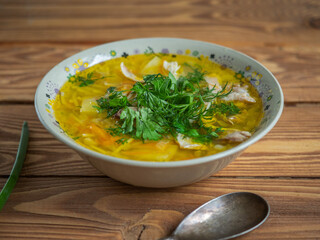 Closeup chicken soup sprinkled with chopped onion feathers in a deep ceramic plate.
