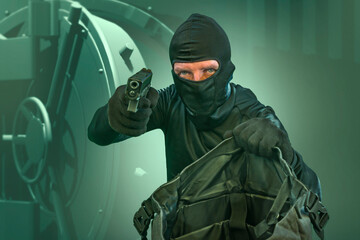 heist and robbery - Hollywood style portrait of man in balaclava mask holding gun in front of security metal vault door in bank or casino heist concept stealing money