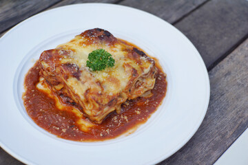 Close up of meat lasagna on a white plate with wooden table background.