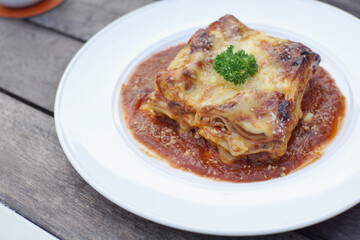 Close up of meat lasagna on a white plate with wooden table background.