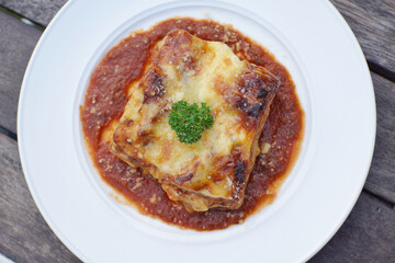 Close up of meat lasagna on a white plate with wooden table background.
