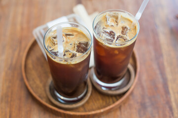 Two iced coffee with glass cups on wooden tray in a coffee shop.