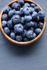  Blueberry berry in a wooden round cup close-up on a black slate background.Healthy bio natural dessert and snack.Vegetarian and vegan food. blueberries season.