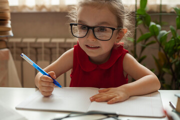 Naklejka na ściany i meble The girl sits in glasses and does homework. International Literacy Day. Education and science. Distance learning. Preschool education.