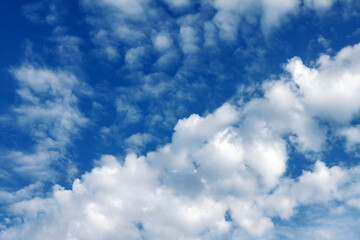 White fluffy cumulus clouds are located in an ascending diagonal image on a cloudy blue sky on a clear summer sunny day.
