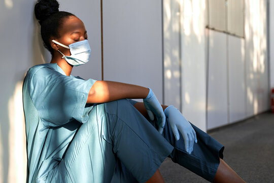 Tired black nurse with mask sitting in hallway