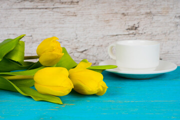 yellow tulips with coffee cup on turquoise wooden table