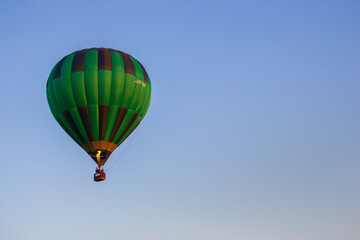 Kyiv, Ukraine - 06/26/2020: Hot air balloon in clear summer sky. Green balloon on blue background with copy space. Bright geometric design. Summer leisure. Hot air balloon in flight.