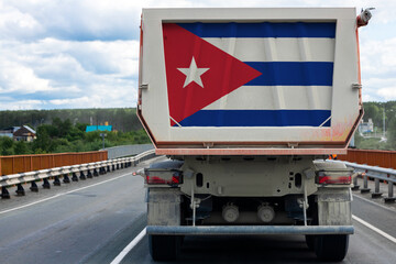 Big dirty truck with the national flag of  Cuba moving on the highway, against the background of the village and forest landscape. Concept of export-import,transportation, national delivery of goods