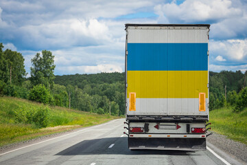 Fototapeta na wymiar A truck with the national flag of Ukraine depicted on the back door carries goods to another country along the highway. Concept of export-import,transportation, national delivery of goods