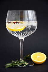 Gin and tonic with lemon and rosemary in crystal glass against the black background